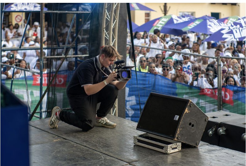 Videographer kneeling on stage filming a large crowd